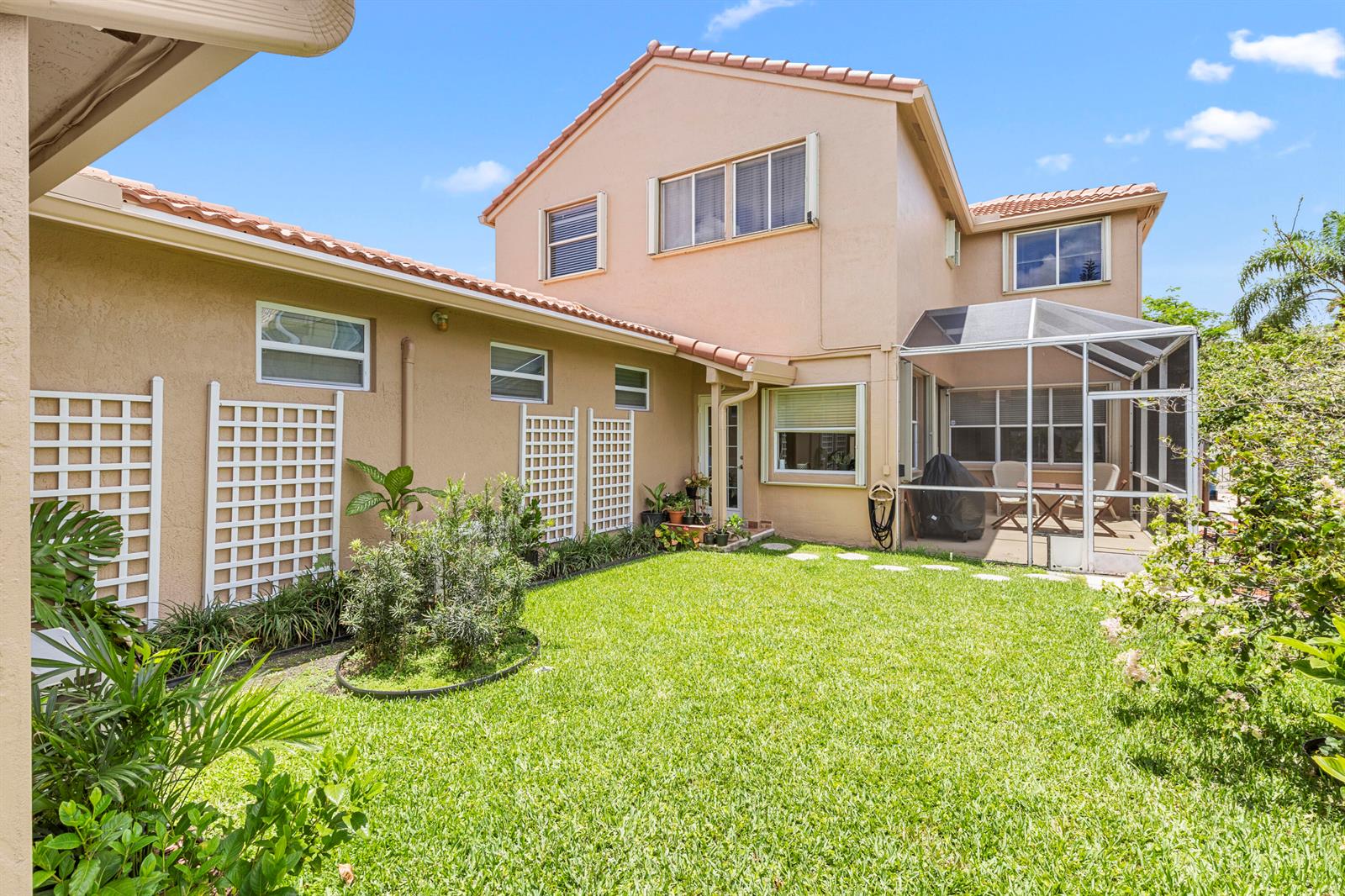 The exterior of a two-story house features a grassy backyard, a screened patio, and trellises — 907 Stanton Drive, Weston FL 33326, WESTON, FL