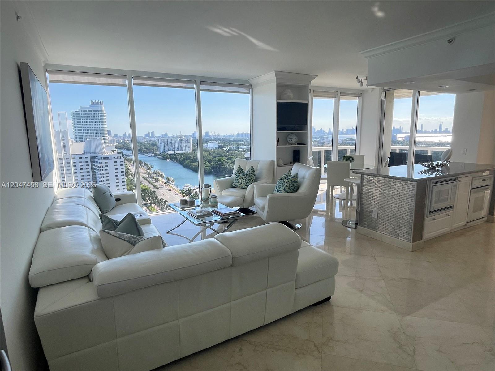 A bright living room features a white sectional sofa, floor-to-ceiling windows, and city views — 4775 Collins Ave # 2305, Miami Beach FL 33140, MIAMI BEACH, FL
