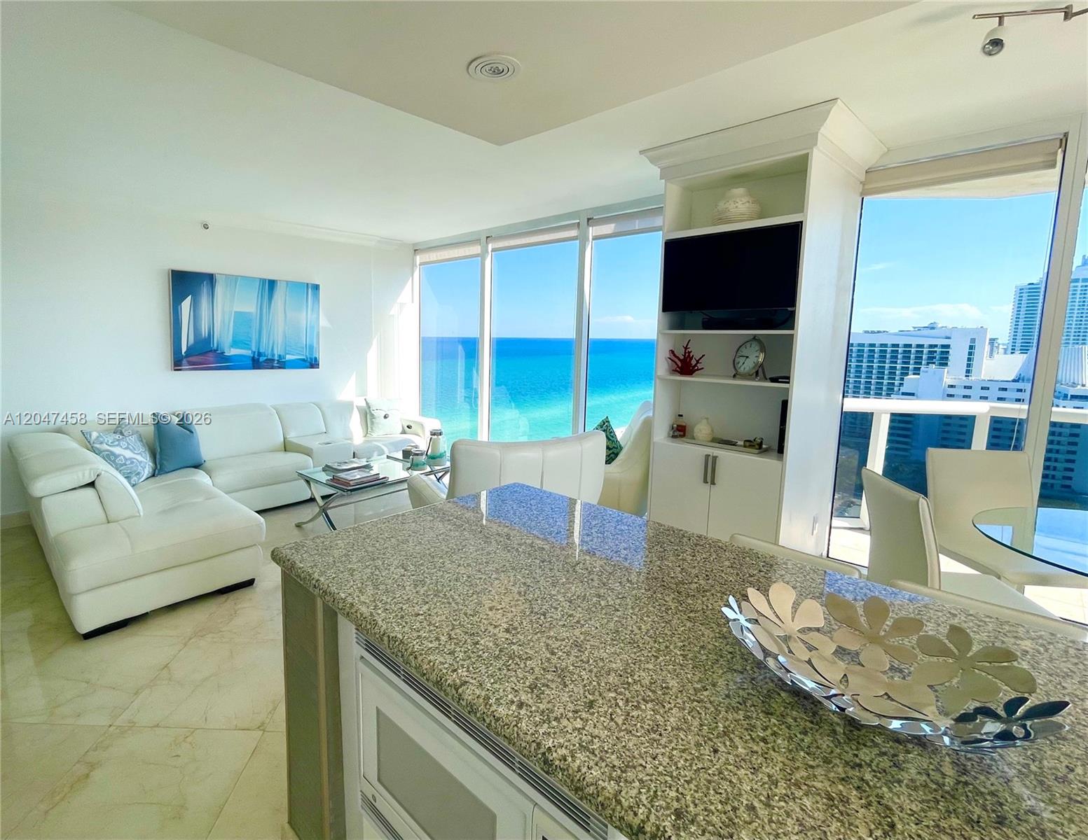 A bright living area features a white sectional sofa, granite kitchen island, and ocean views — 4775 Collins Ave # 2305, Miami Beach FL 33140, MIAMI BEACH, FL