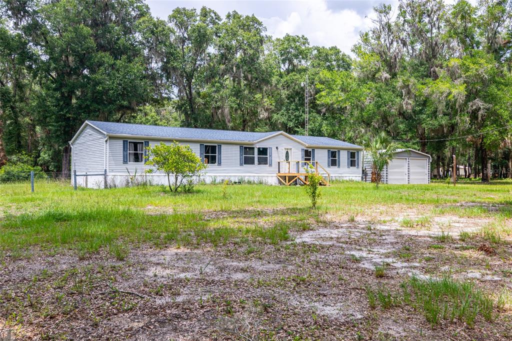 A single-story manufactured home with light siding stands on a grassy lot with trees — 19050 NE 3RD COURT, CITRA, FL