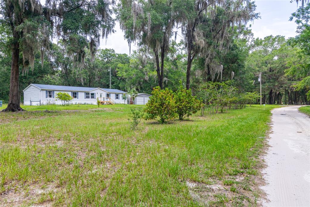 A single-story manufactured home sits on a grassy lot surrounded by moss-draped trees — 19050 NE 3RD COURT, CITRA, FL