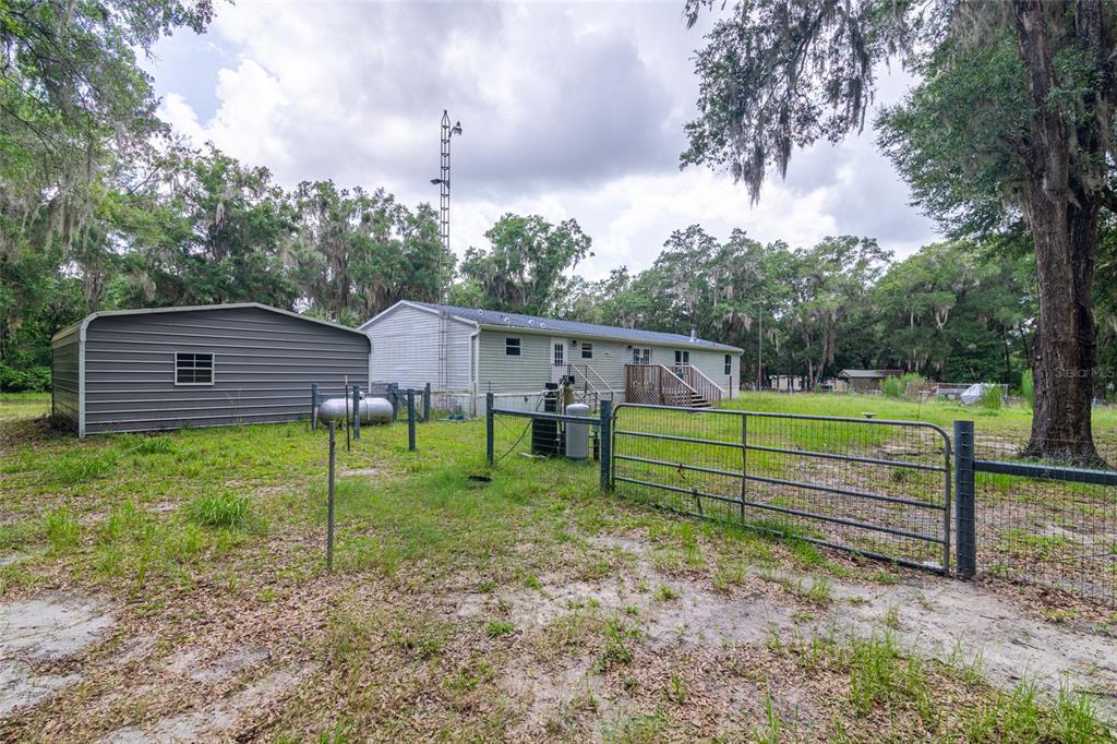 A metal shed and a manufactured home sit on a grassy lot with trees — 19050 NE 3RD COURT, CITRA, FL