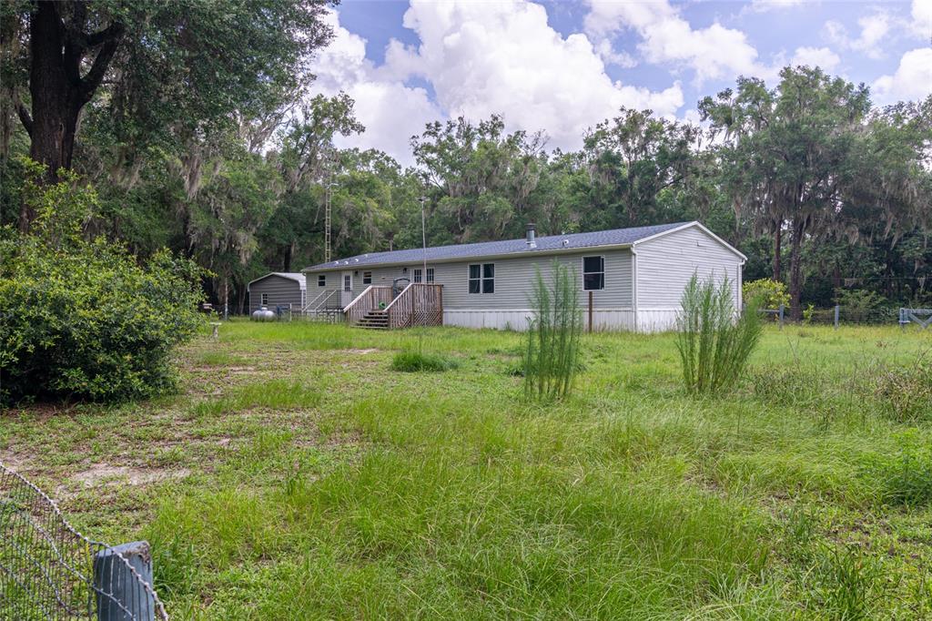 A single-story manufactured home with light gray siding sits on a grassy, wooded lot — 19050 NE 3RD COURT, CITRA, FL