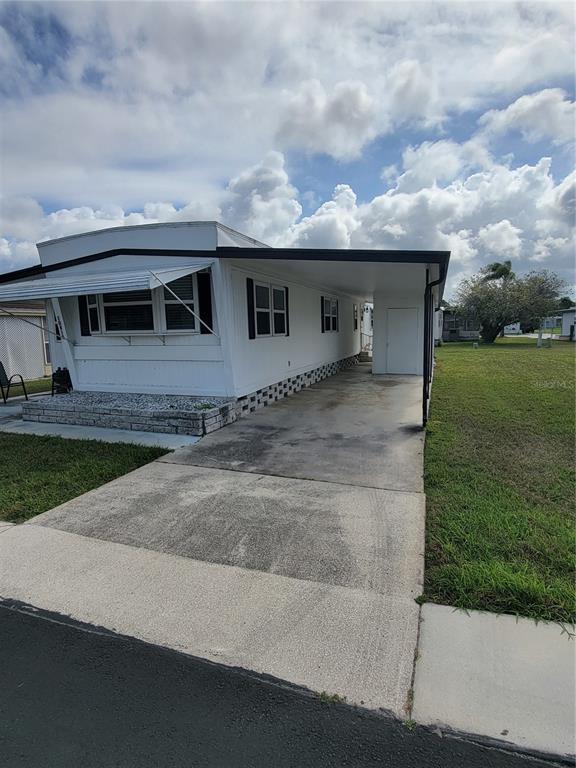 A white mobile home features a concrete driveway, a carport, and a small front patio — 10810 TIOGA DRIVE, PORT RICHEY, FL
