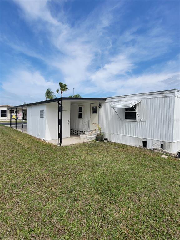 A white mobile home with a covered carport and a small concrete patio entrance — 10810 TIOGA DRIVE, PORT RICHEY, FL