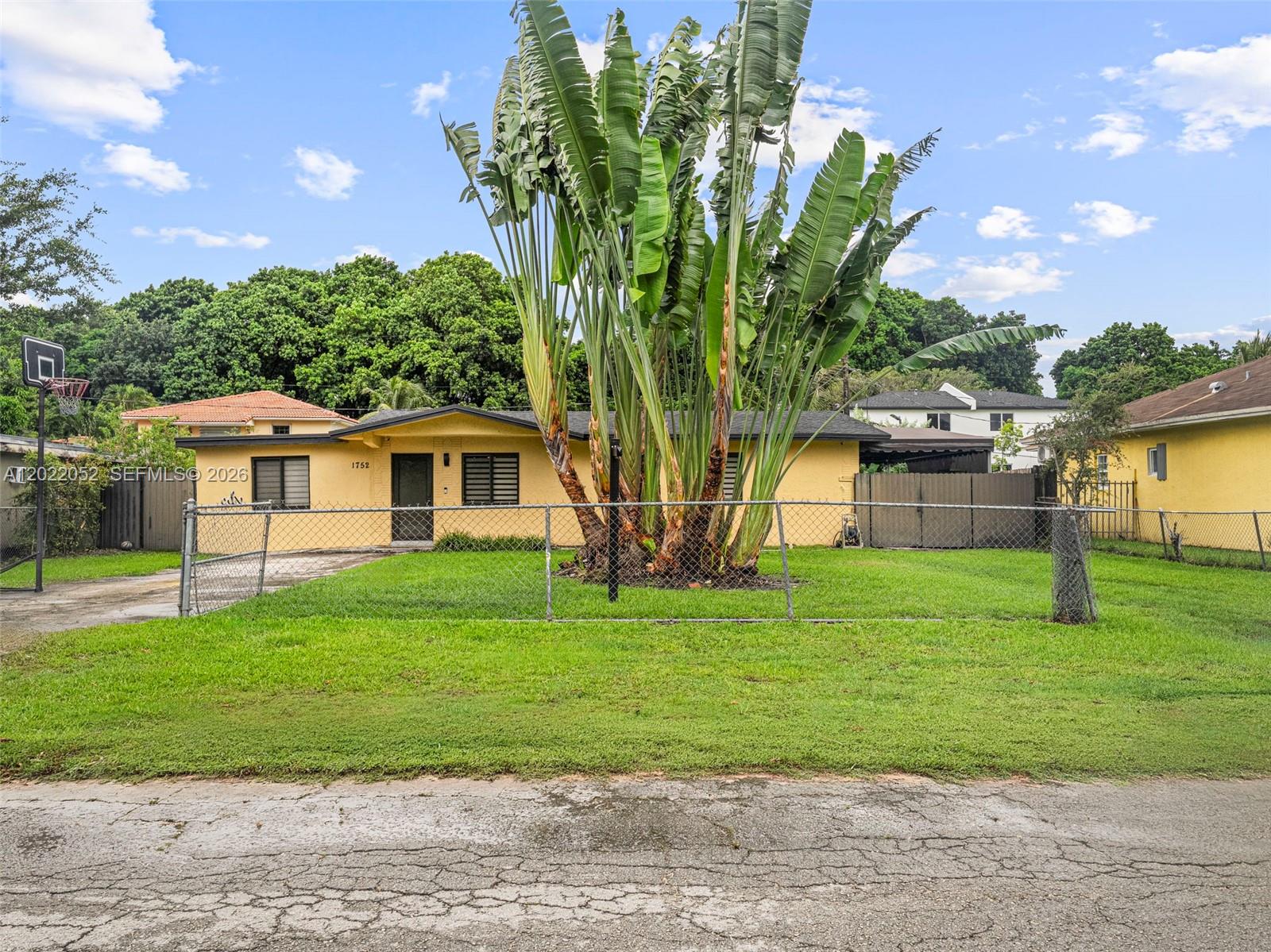 A yellow single-story house features a large palm plant in the fenced front yard — 1752 NW 108th St, Miami FL 33167, MIAMI, FL
