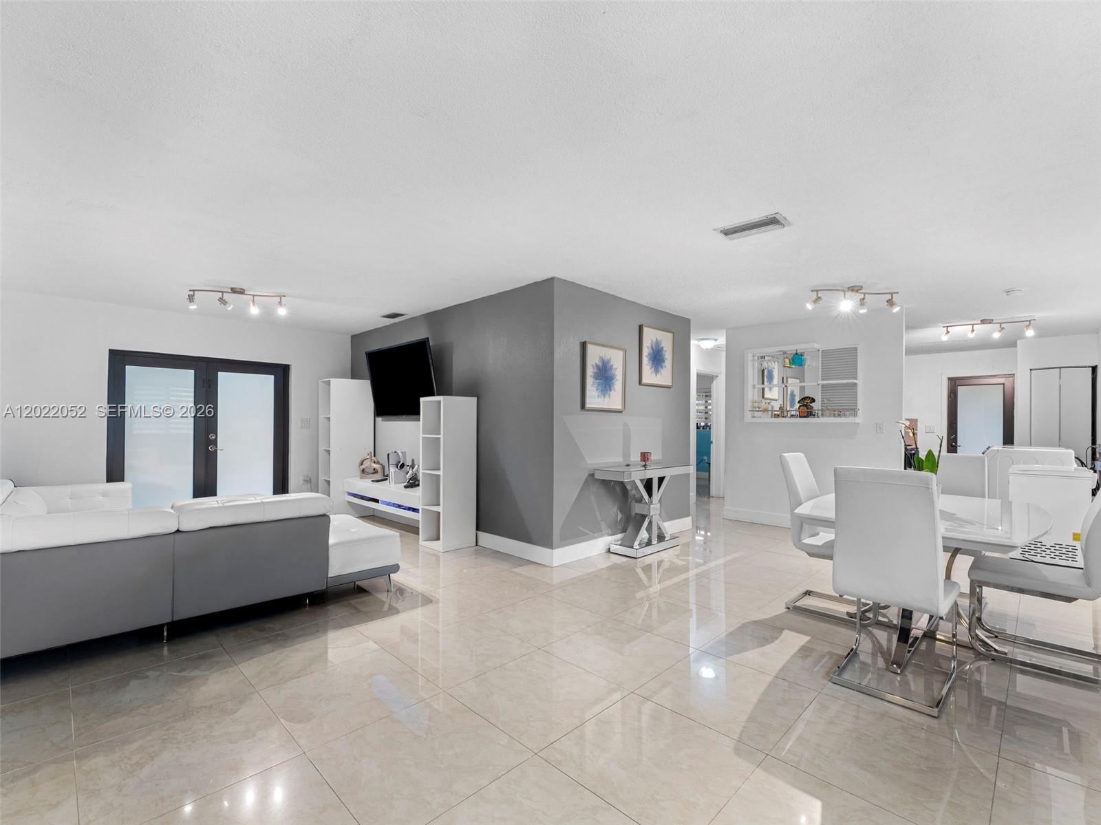 A modern living and dining area features white tile floors, a gray accent wall, and furniture — 1752 NW 108th St, Miami FL 33167, MIAMI, FL