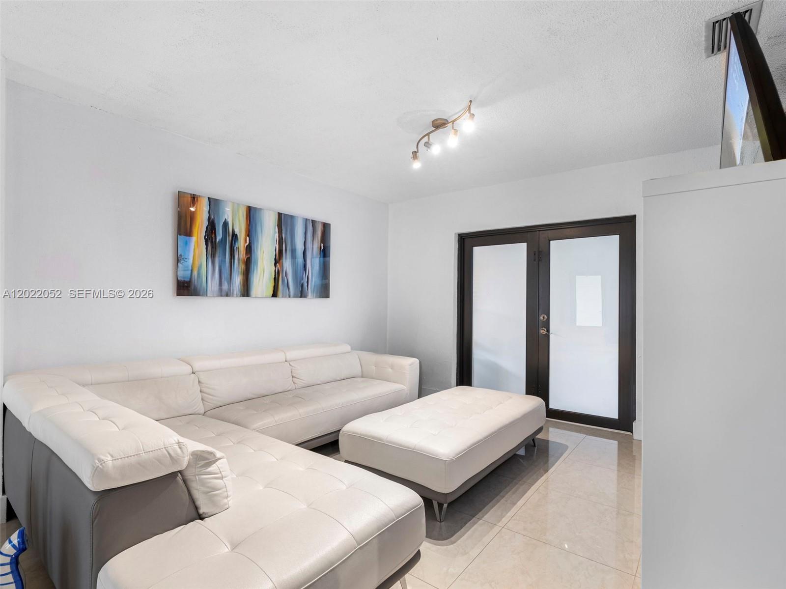 A living room features a white sectional sofa, a matching ottoman, and glass-paneled double doors — 1752 NW 108th St, Miami FL 33167, MIAMI, FL