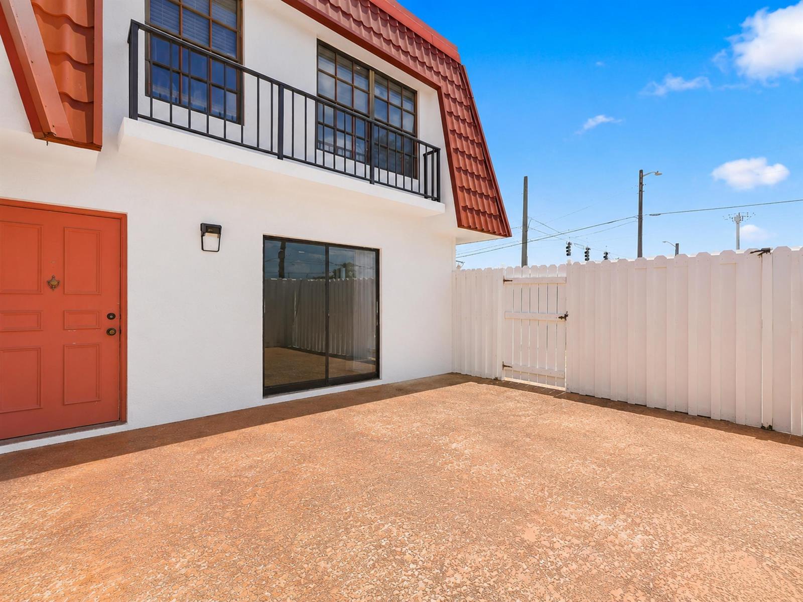 A white building exterior features a red door, a balcony, and a fenced patio area — 2716 Yale Lane, Boynton Beach FL 33426, BOYNTON BEACH, FL
