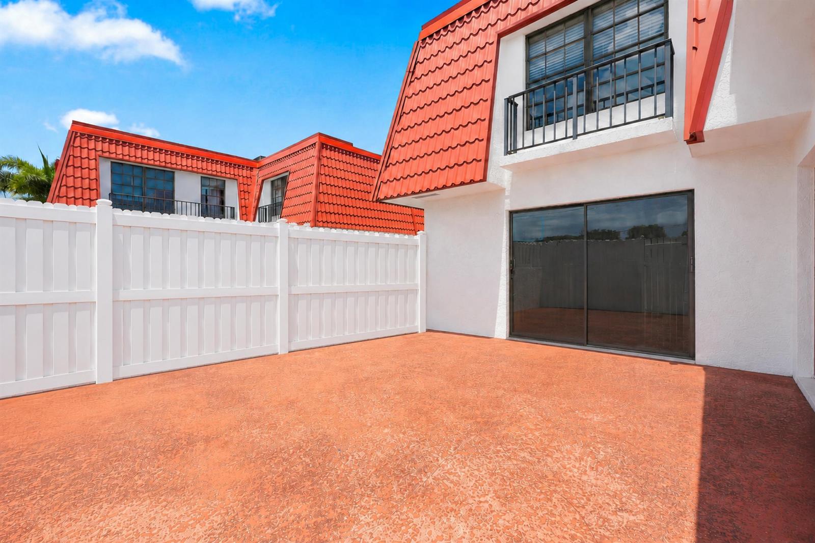 A white vinyl fence encloses a red concrete patio next to a white building — 2716 Yale Lane, Boynton Beach FL 33426, BOYNTON BEACH, FL