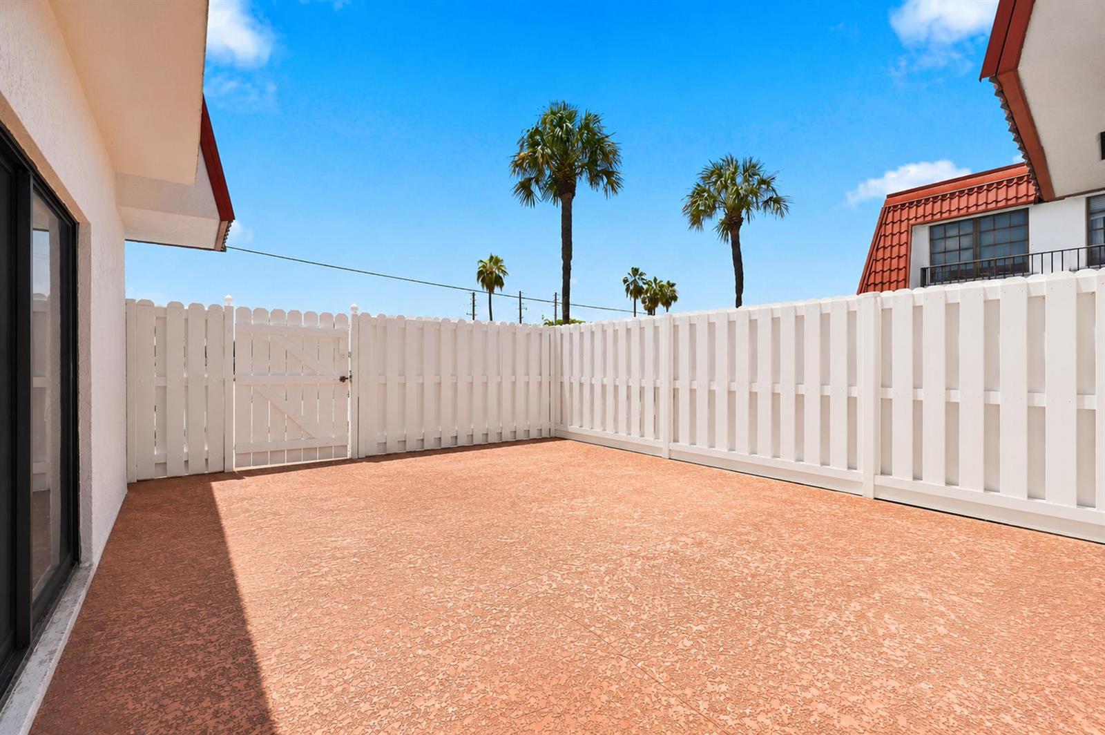 A private patio with a textured orange floor and white vinyl fencing under a blue sky — 2716 Yale Lane, Boynton Beach FL 33426, BOYNTON BEACH, FL