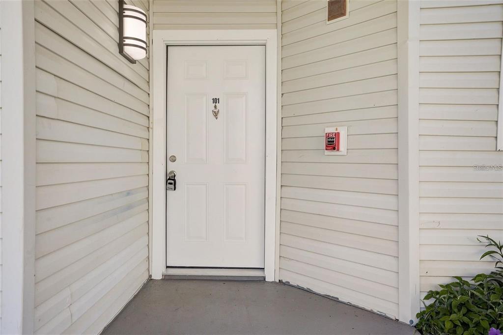 A white front door with a lockbox and fire alarm pull station on beige siding — 2556 WOODGATE BOULEVARD UNIT 101, ORLANDO, FL