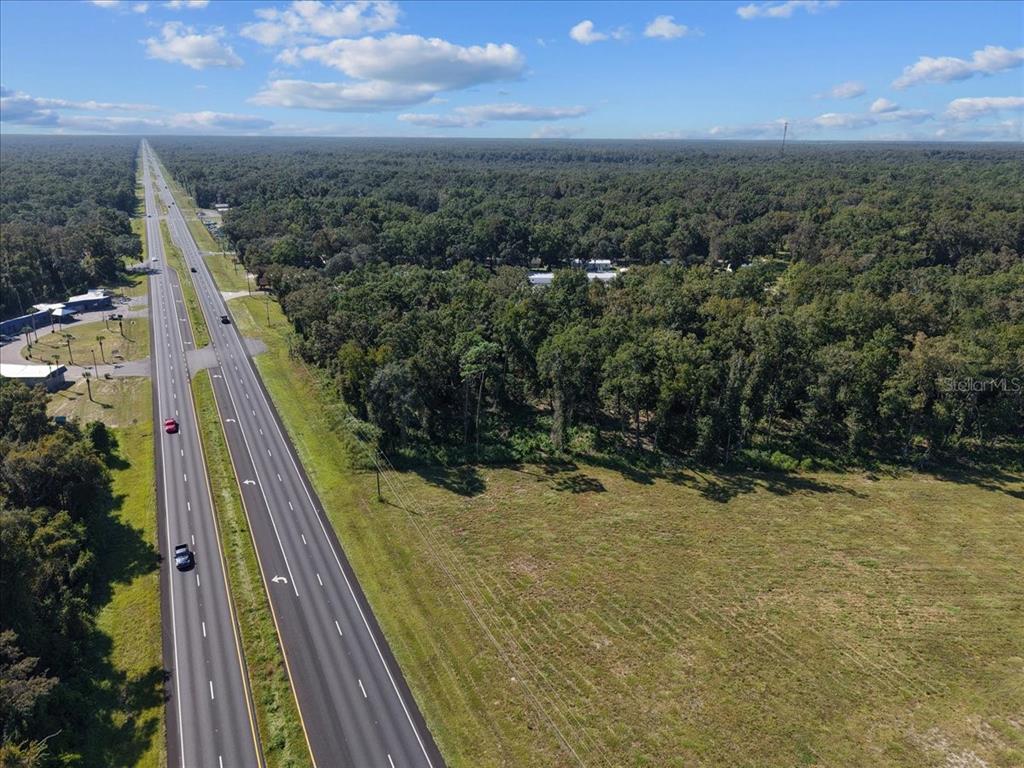 An aerial view shows a multi-lane highway running alongside a large, undeveloped grassy field — NW US 19 HIGHWAY, FANNING SPRINGS, FL