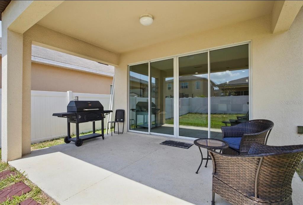 A covered concrete patio features a grill, outdoor furniture, and sliding glass doors — 914 FALLON HILLS DRIVE, HAINES CITY, FL