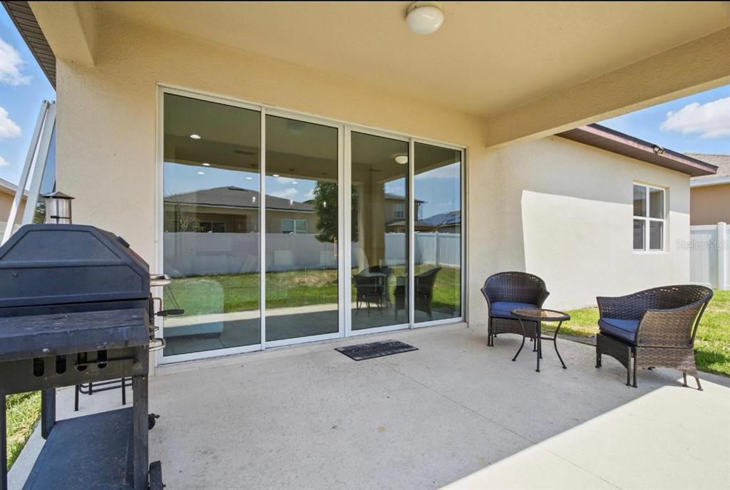 A covered concrete patio features a sliding glass door, a grill, and outdoor wicker furniture — 914 FALLON HILLS DRIVE, HAINES CITY, FL