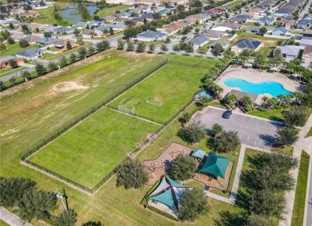 An aerial view shows a community park with a swimming pool, playground, and soccer field — 914 FALLON HILLS DRIVE, HAINES CITY, FL