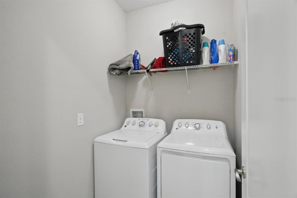 A laundry room features a white washer and dryer beneath a wire storage shelf — 914 FALLON HILLS DRIVE, HAINES CITY, FL