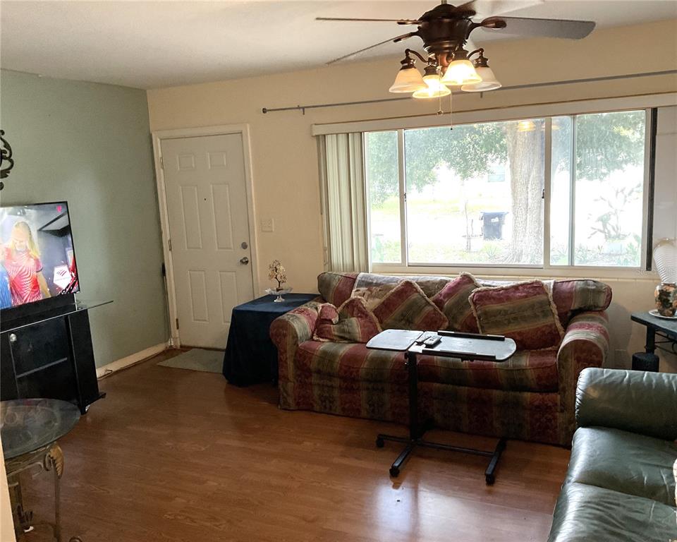 A living room features wood-look flooring, a patterned sofa, a ceiling fan, and a large window — 416 CRABTREE AVENUE, ORLANDO, FL