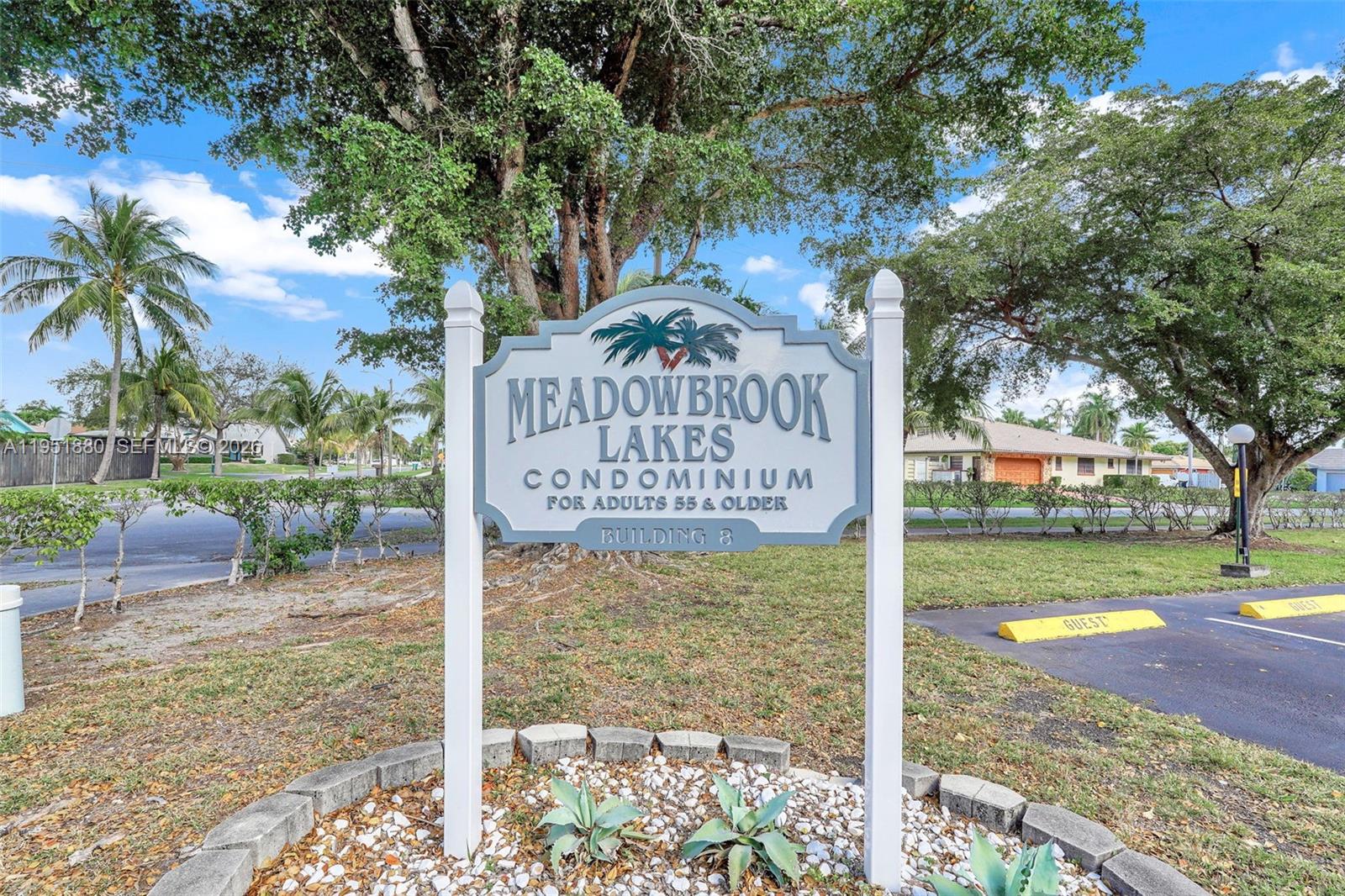 A sign for Meadowbrook Lakes Condominium for adults 55 and older stands outdoors — 314 SE 10th St # 103, Dania Beach FL 33004, DANIA BEACH, FL