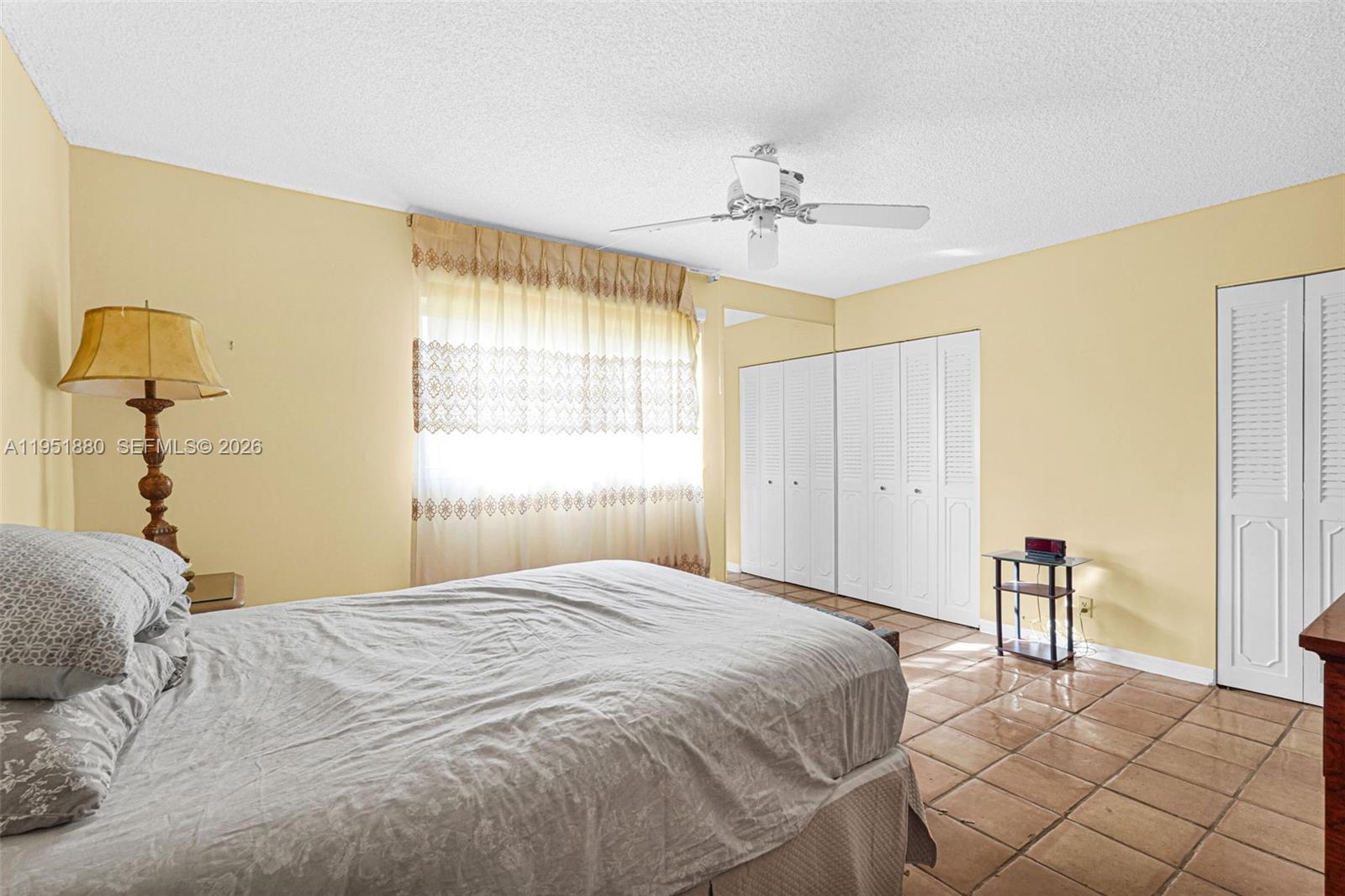 A bedroom features yellow walls, a ceiling fan, tile flooring, and white louvered closet doors — 314 SE 10th St # 103, Dania Beach FL 33004, DANIA BEACH, FL