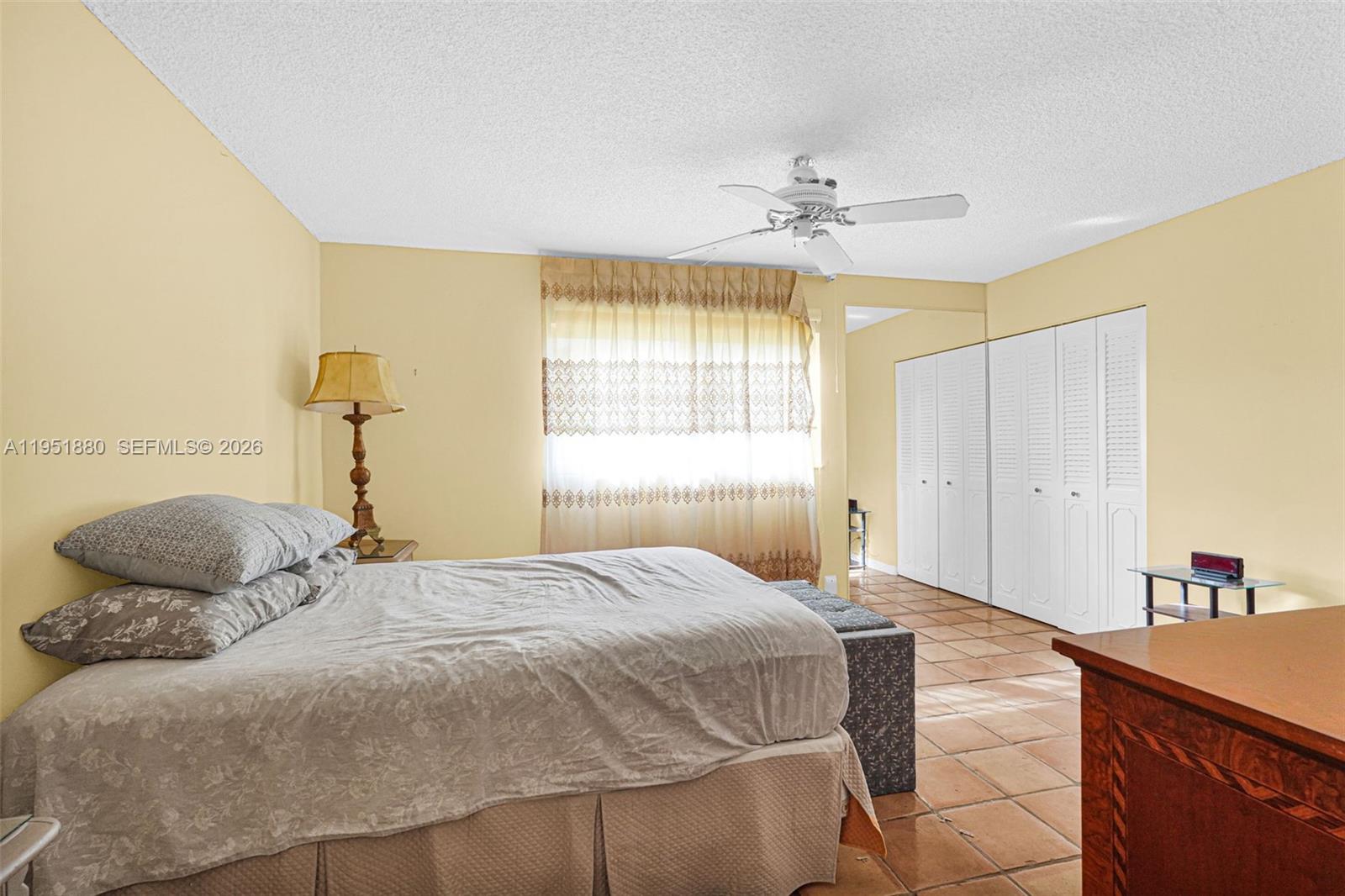 A bedroom features a bed, tiled floors, white louvered closet doors, and a ceiling fan — 314 SE 10th St # 103, Dania Beach FL 33004, DANIA BEACH, FL
