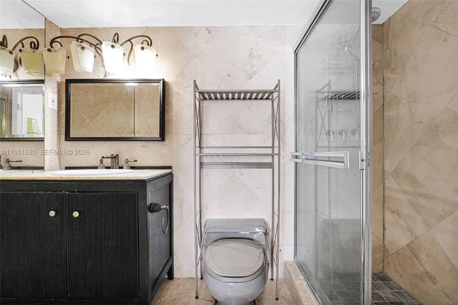 A bathroom features a black vanity, a toilet with a metal rack, and a glass shower — 314 SE 10th St # 103, Dania Beach FL 33004, DANIA BEACH, FL
