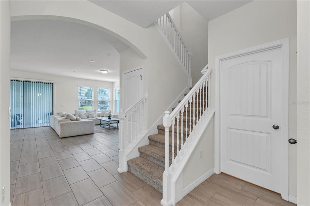 An entryway features a carpeted staircase with white railings, tile flooring, and an arched opening — 16495 POINT ROCK DRIVE, WINTER GARDEN, FL