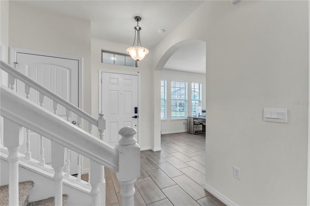 An entryway features a white staircase, tile flooring, a pendant light, and an arched doorway — 16495 POINT ROCK DRIVE, WINTER GARDEN, FL