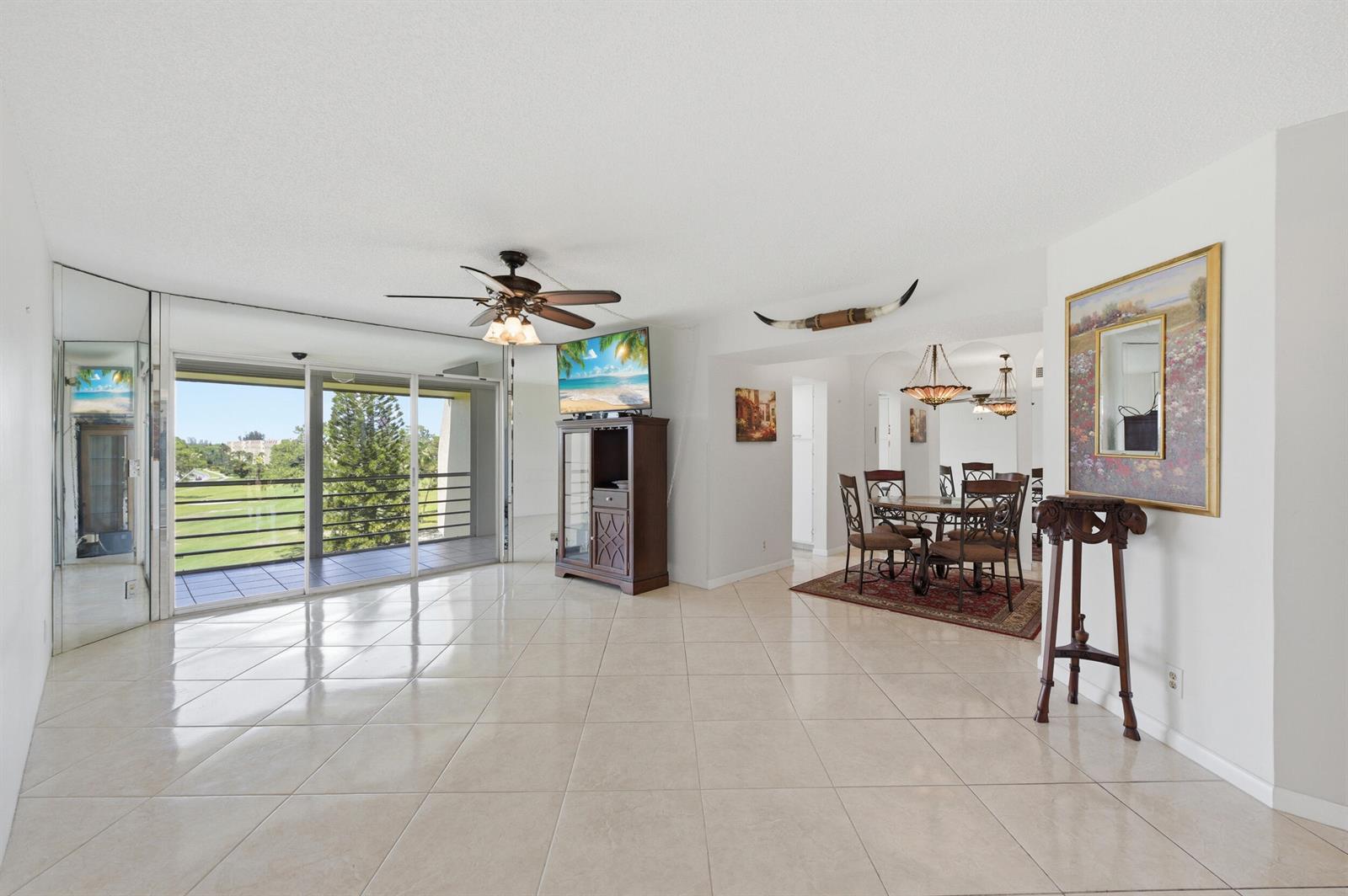 A bright living and dining area features tile floors, a ceiling fan, and balcony access — 3836 Via Poinciana # 603, FL 33467, FL