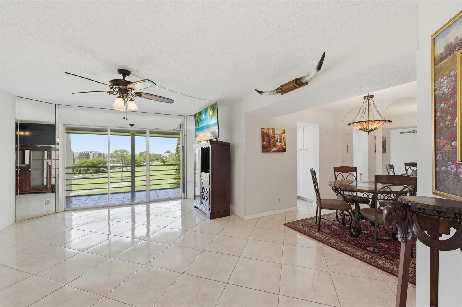 A living and dining area with tile floors, a ceiling fan, and a balcony view — 3836 Via Poinciana # 603, FL 33467, FL