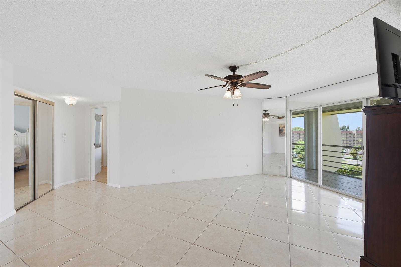 An empty living room with tile floors, a ceiling fan, mirrored closet doors, and a balcony — 3836 Via Poinciana # 603, FL 33467, FL