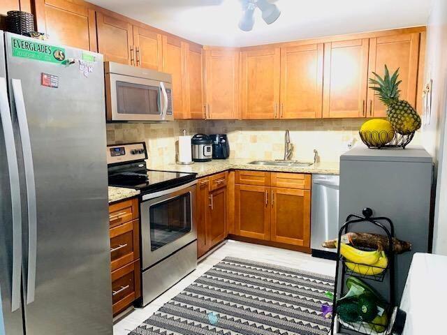 A kitchen features wooden cabinets, stainless steel appliances, a patterned rug, and a fruit basket — 737 SE 1st Way # 306, Deerfield Beach FL 33441, DEERFIELD BEACH, FL