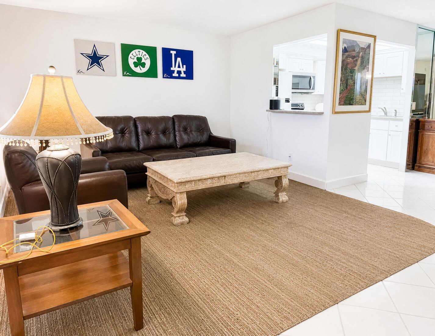 A living room features a brown leather sofa, a stone coffee table, and sports wall art — 6 Brittany A # 6a, Delray Beach FL 33446, DELRAY BEACH, FL