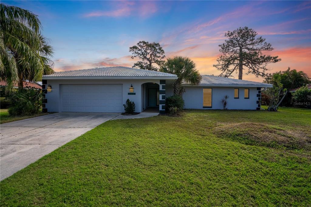 A single-story house with a white exterior, tiled roof, and attached garage under a sunset sky — 2544 CARLISLE PLACE, SARASOTA, FL