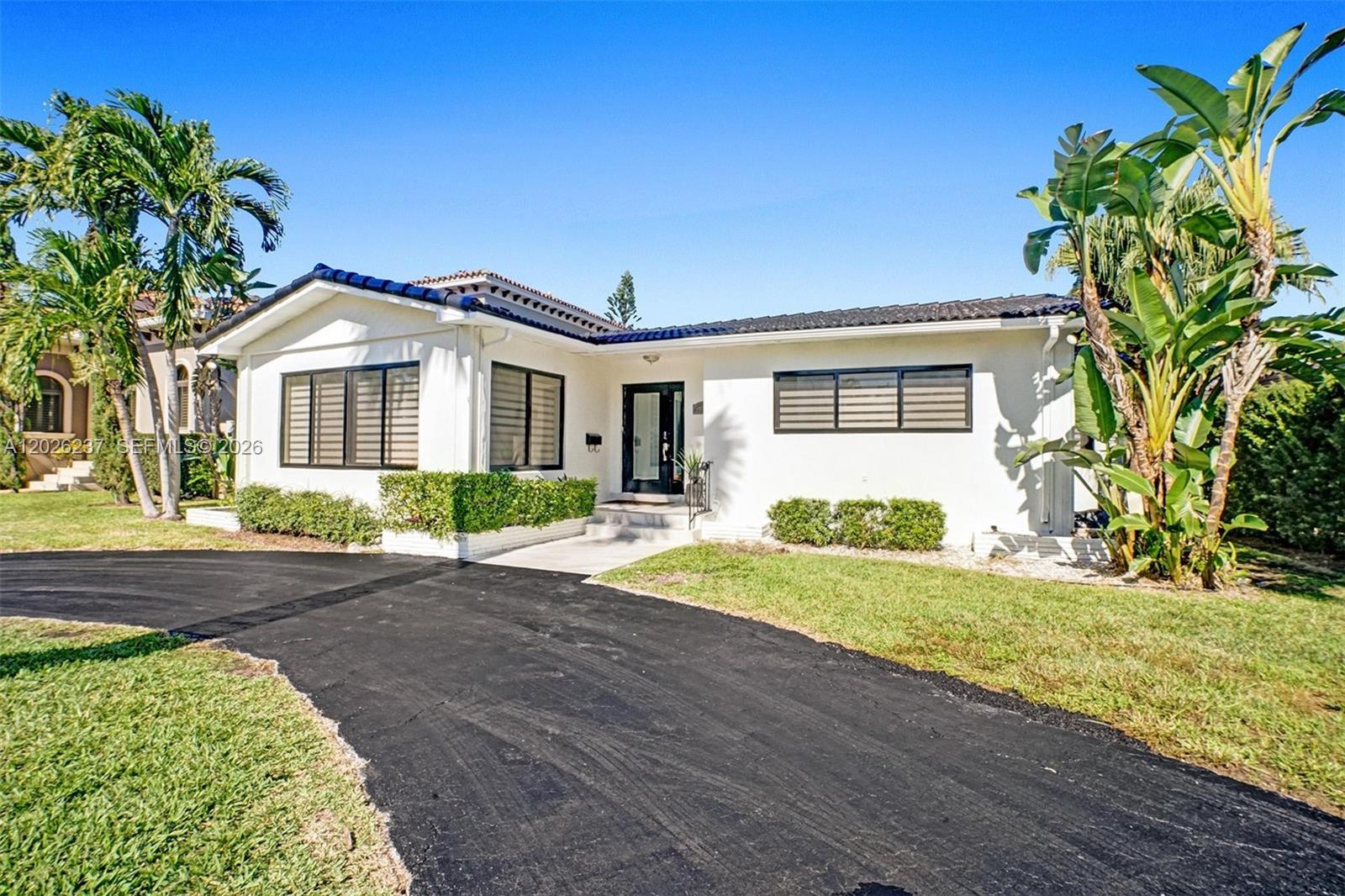 A white single-story house with a black roof and driveway sits under a clear sky — 1355 Madison St, Hollywood FL 33019, HOLLYWOOD, FL