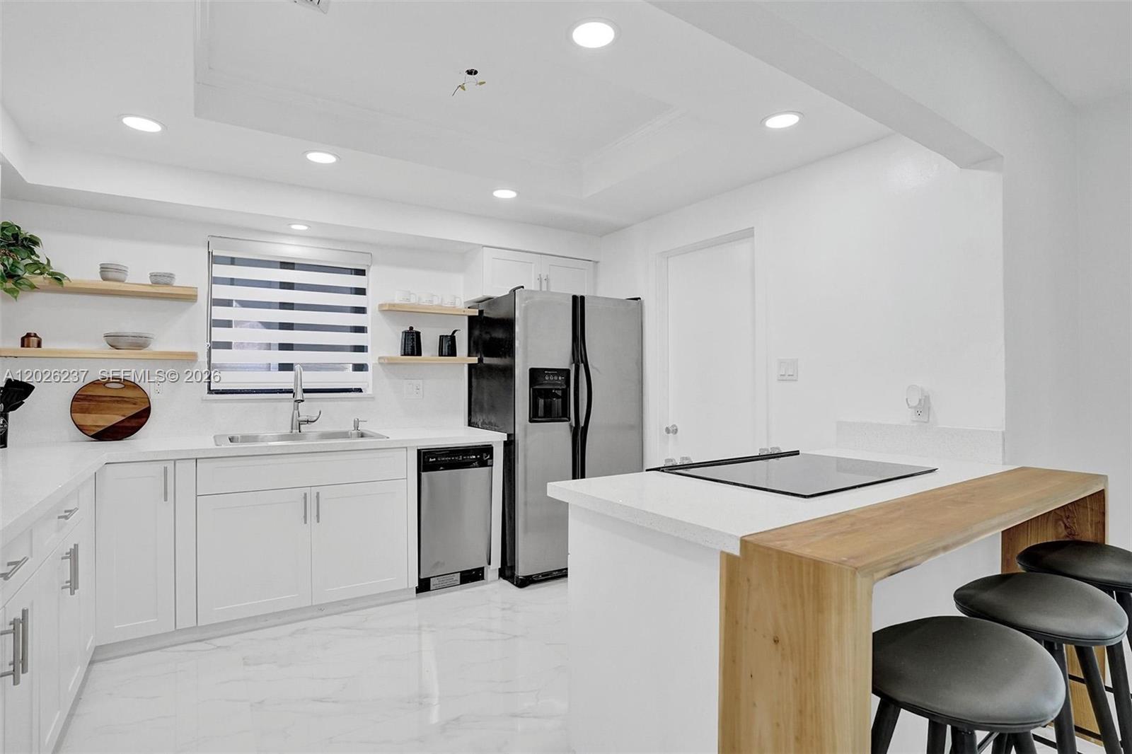 A modern kitchen features white cabinets, stainless steel appliances, and a wooden breakfast bar — 1355 Madison St, Hollywood FL 33019, HOLLYWOOD, FL