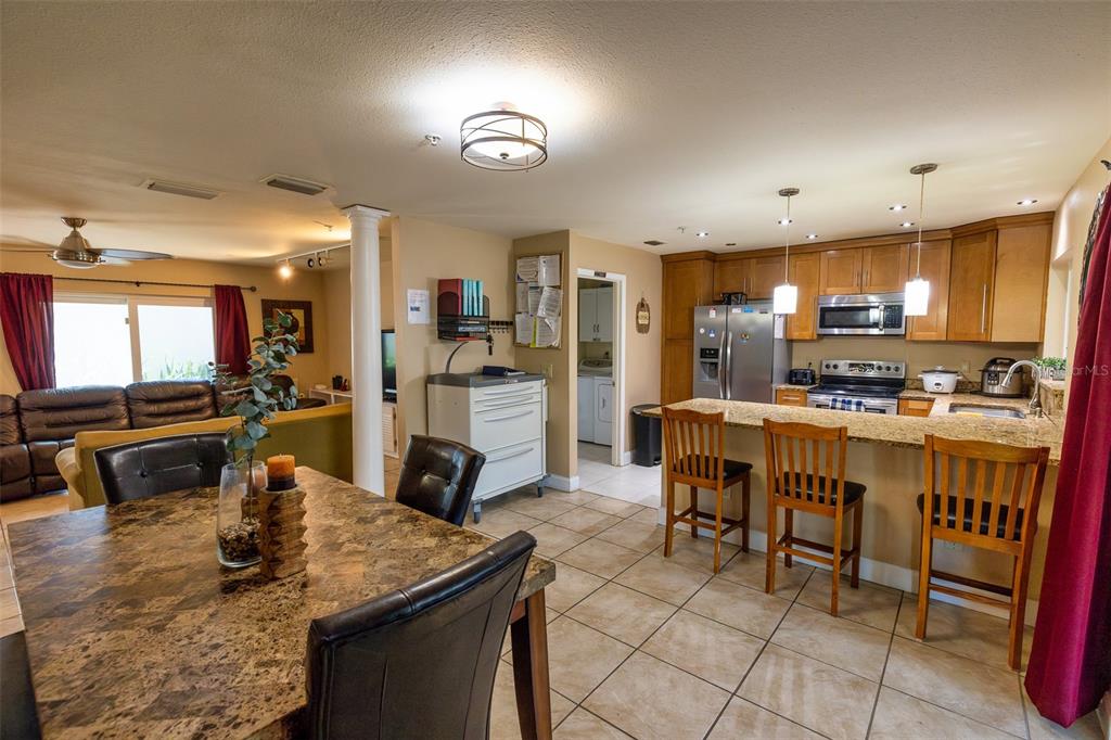An open-concept kitchen and dining area features granite countertops, wooden cabinets, and tile flooring — 7128 WRENWOOD CIRCLE, TAMPA, FL
