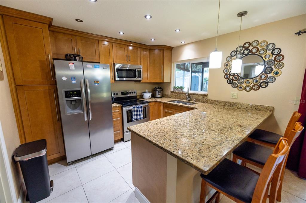 A kitchen with wood cabinets, granite countertops, stainless steel appliances, and a breakfast bar — 7128 WRENWOOD CIRCLE, TAMPA, FL