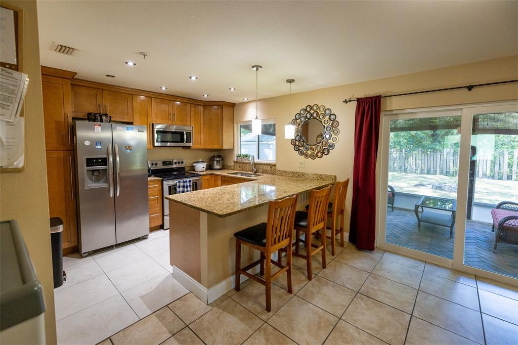 A kitchen with wood cabinets, granite countertops, a breakfast bar, and sliding glass patio doors — 7128 WRENWOOD CIRCLE, TAMPA, FL
