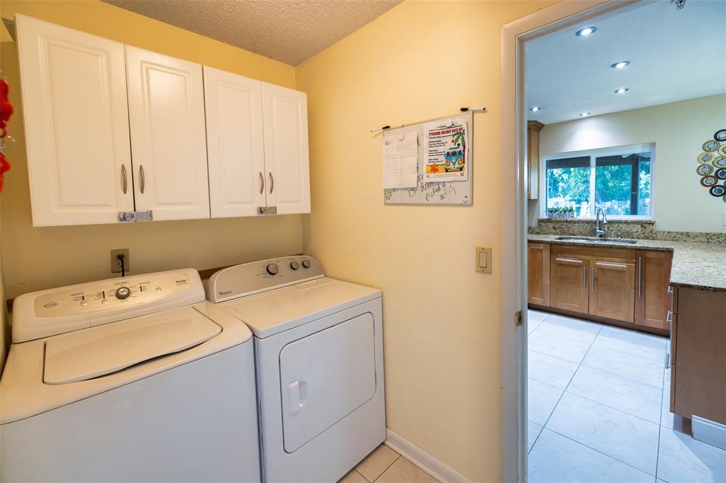 A laundry room with white appliances and cabinets, leading into a kitchen with wood cabinetry — 7128 WRENWOOD CIRCLE, TAMPA, FL