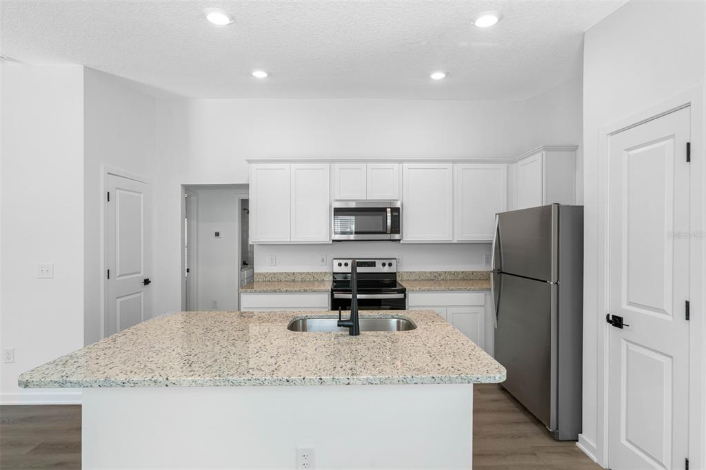 A kitchen features white cabinets, granite countertops, a central island with a sink, and stainless appliances — 5220 WENDAL STREET, SPRING HILL, FL