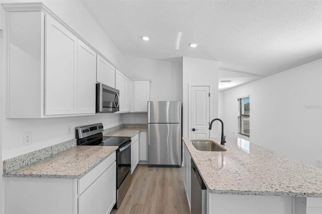 A modern kitchen features white cabinets, granite countertops, stainless steel appliances, and a center island — 5220 WENDAL STREET, SPRING HILL, FL