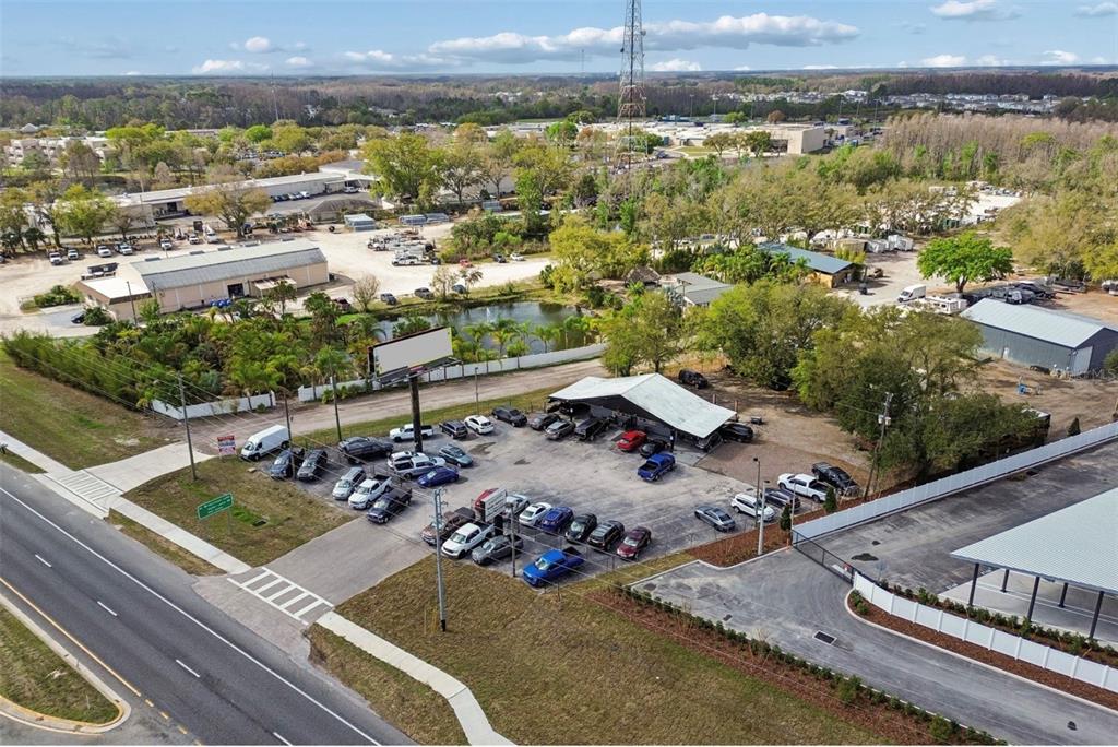 An aerial view shows a car dealership lot with a covered structure and parked vehicles — 7411 LAND O LAKES BOULEVARD, LAND O LAKES, FL