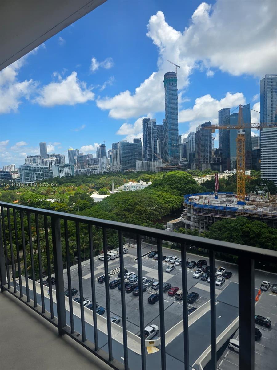 A balcony overlooks a parking lot, green trees, and a city skyline with construction cranes — 1901 Brickell Ave # B1614, Miami FL 33129, MIAMI, FL