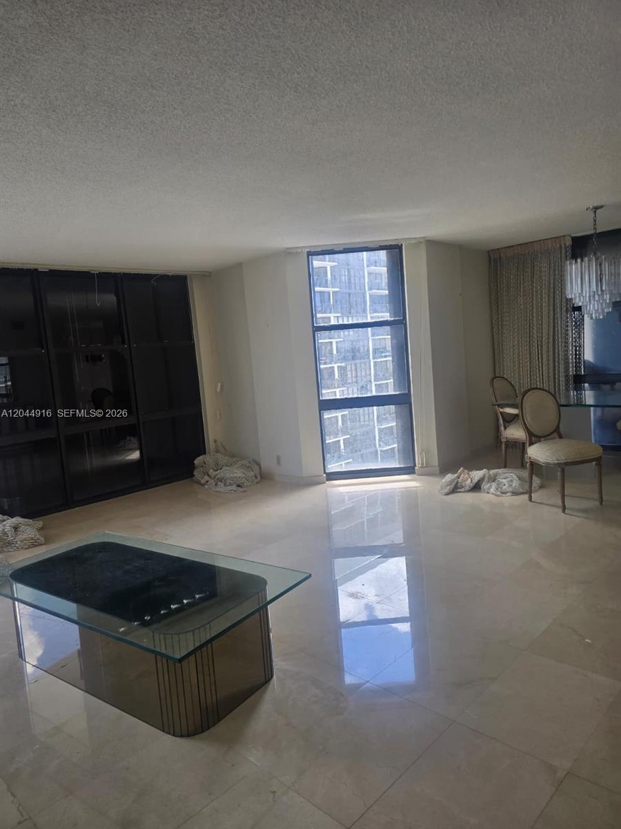 A living room features light tile flooring, a glass coffee table, and a tall window — 1901 Brickell Ave # B1614, Miami FL 33129, MIAMI, FL