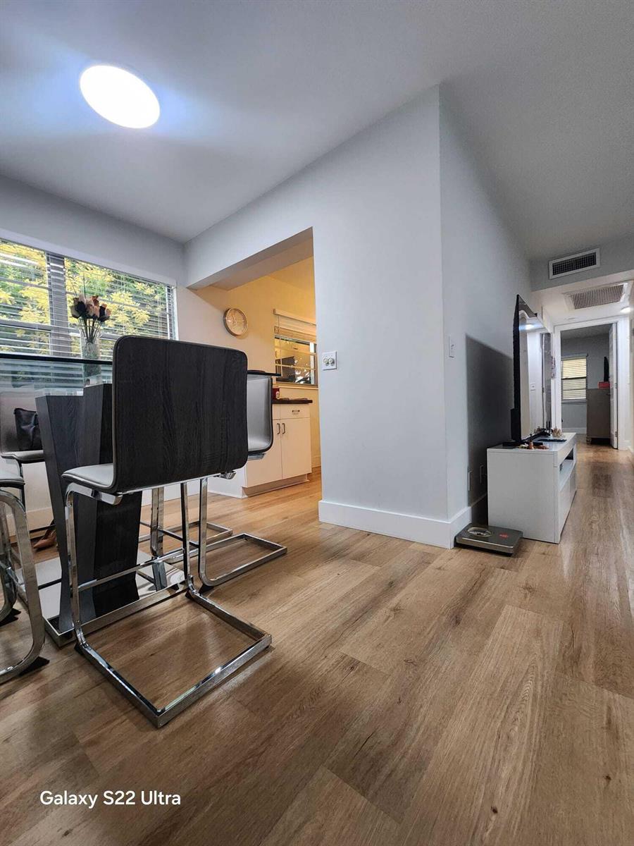 A dining area with modern chairs and wood-look flooring leads into a kitchen and hallway — 124 Oakridge I # 124, Deerfield Beach FL 33442, DEERFIELD BEACH, FL