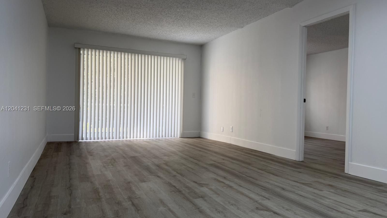 An empty room features white walls, wood-look flooring, and a sliding glass door with blinds — 237 Lake Frances Dr # 237, West Palm Beach FL 33411, WEST PALM BEACH, FL