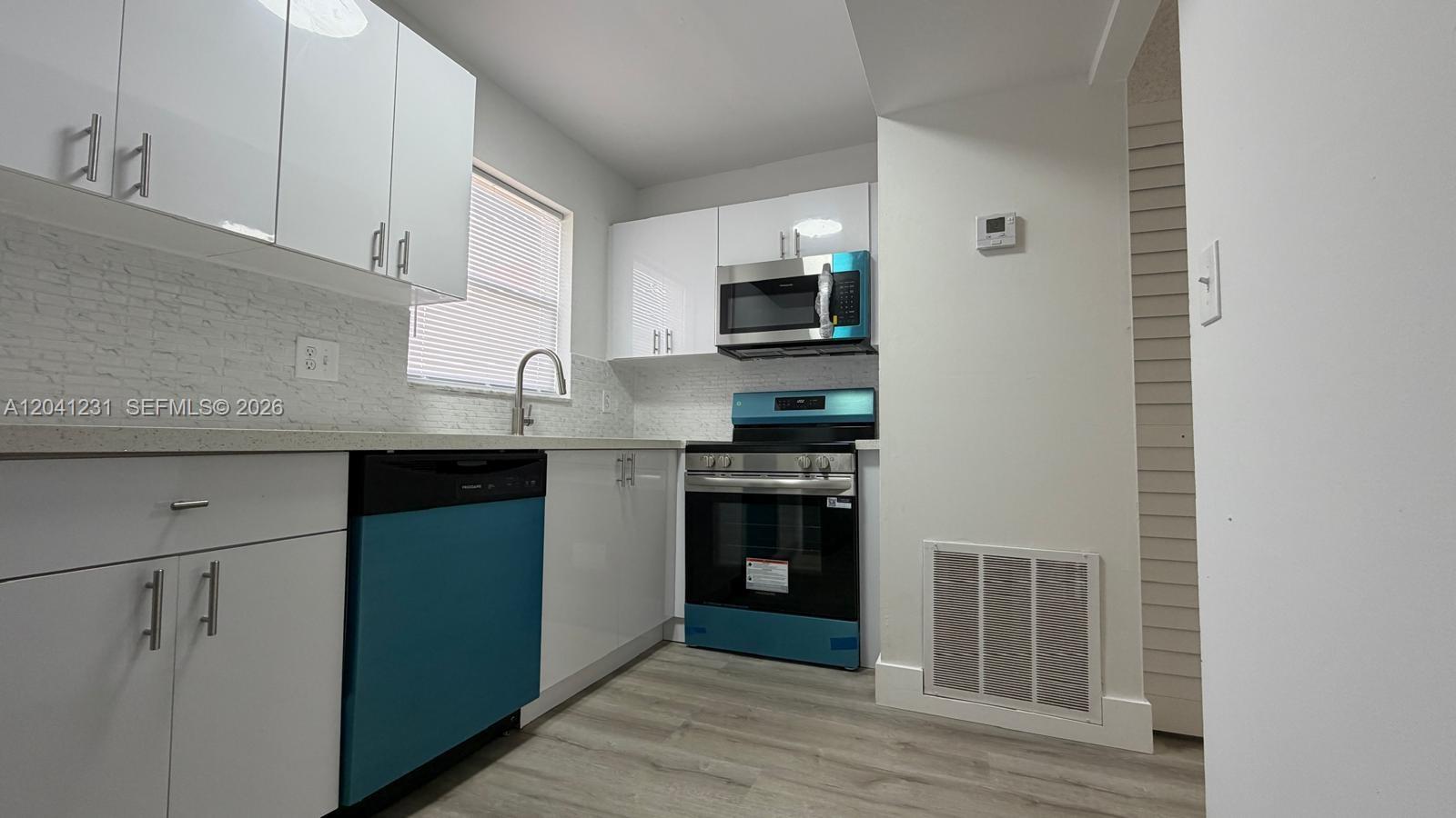 A modern kitchen features white cabinets, stainless steel appliances, and light wood-look flooring — 237 Lake Frances Dr # 237, West Palm Beach FL 33411, WEST PALM BEACH, FL