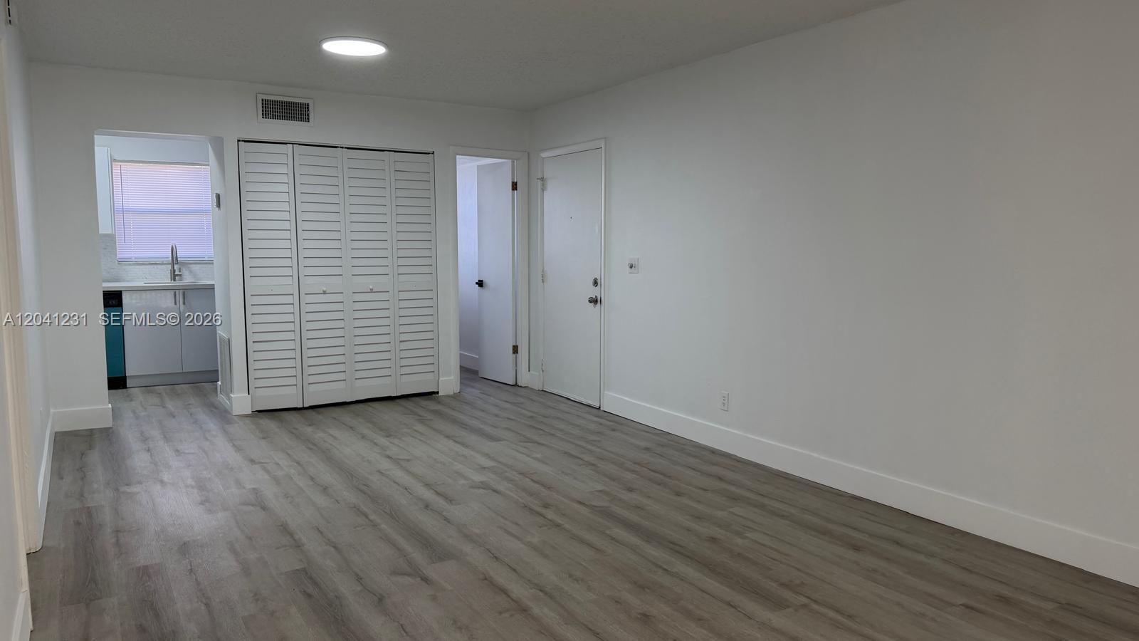 A room with gray wood-look flooring, white walls, a closet, and an adjacent kitchen — 237 Lake Frances Dr # 237, West Palm Beach FL 33411, WEST PALM BEACH, FL