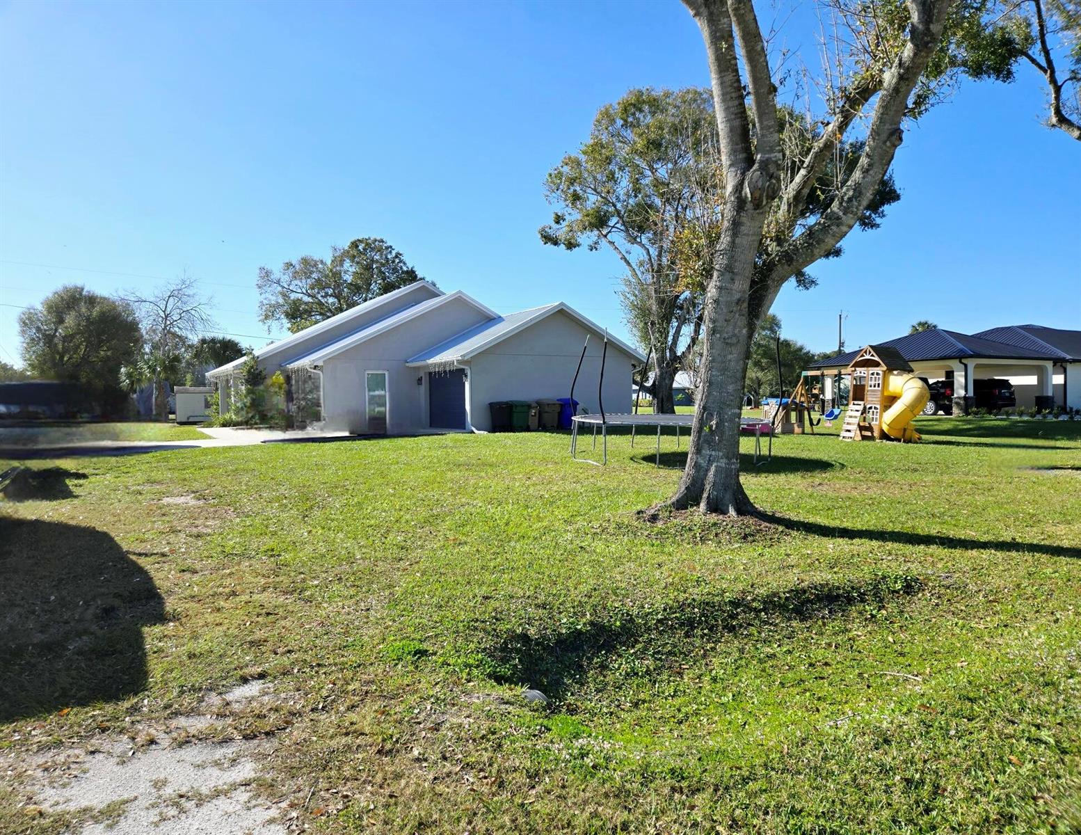 A view of a house exterior with a large lawn, a trampoline, and a playset — 603 NW 11th Avenue, Okeechobee FL 34972, OKEECHOBEE, FL